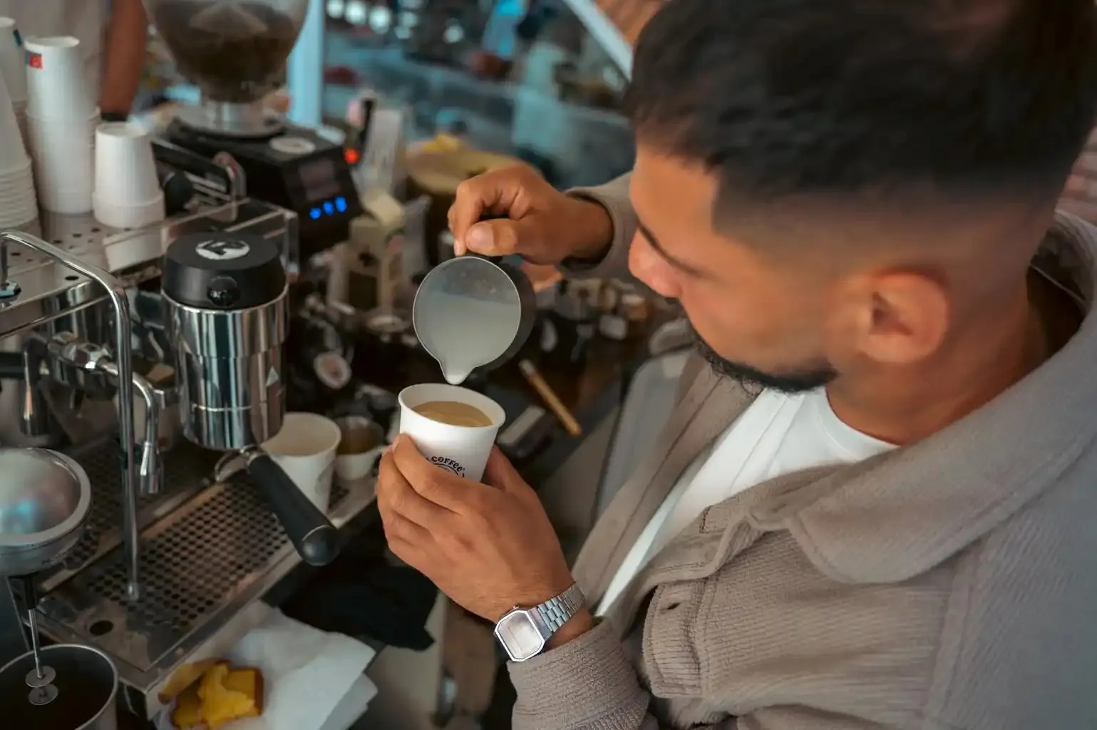 Cristian turnând lapte pentru latte art într-un pahar Zoe Coffee