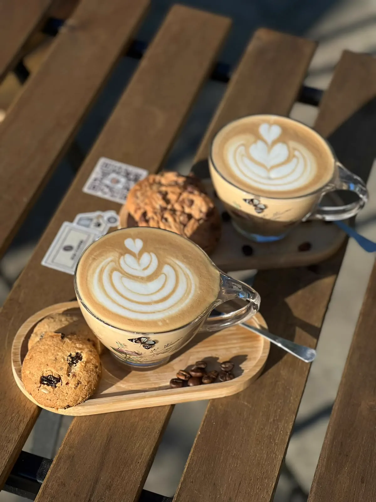 Două cappuccino cu latte art și fursecuri pe o tavă de lemn